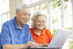 Senior Chinese Couple Sitting At Desk Using Laptop At Home