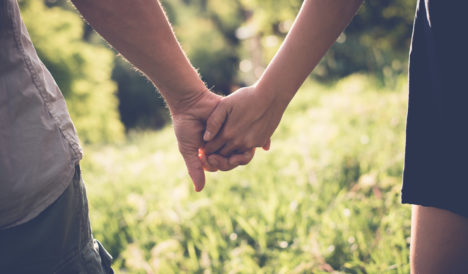 Young couple in love walking in the summer park holding hands, filtered image