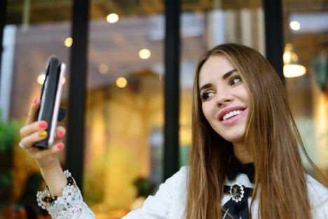 Woman with long hair sitting outside, taking a selfie.