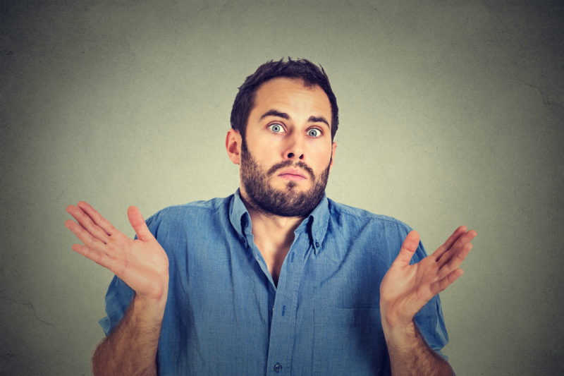 Closeup portrait young man shrugging shoulders who cares so what I don't know gesture isolated on grey wall background. Body language